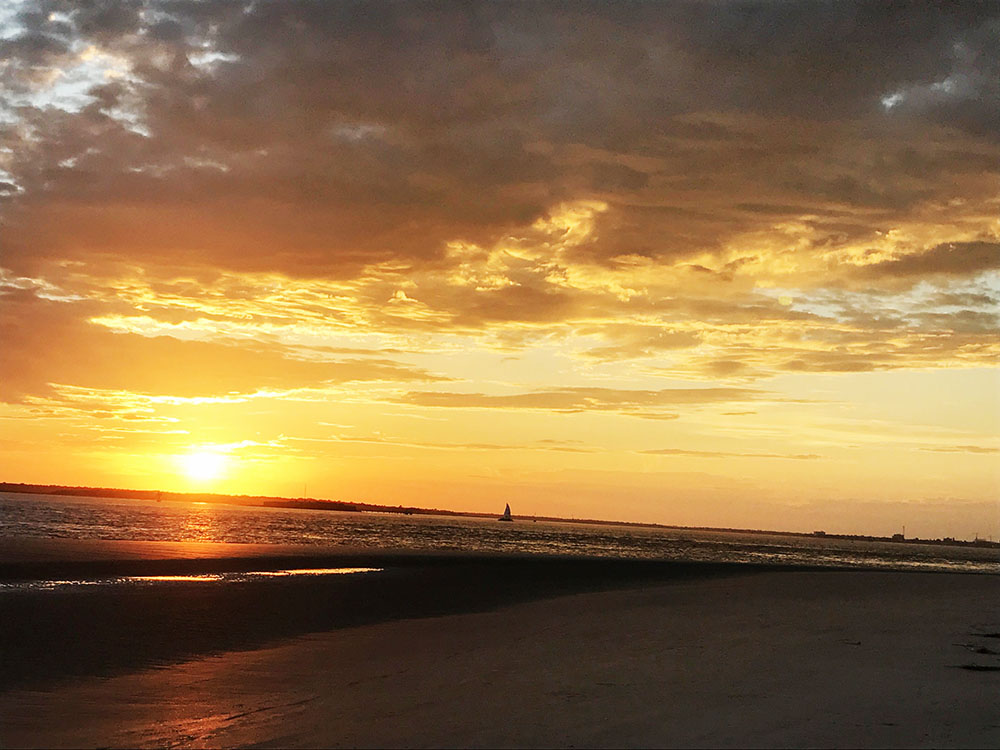 Sunset on Sullivan's Island overlooking the city with a sailboat in the distance